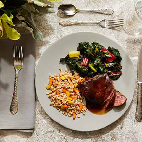 table setting with a white plate that has tenderloin, rice, and assorted veggies